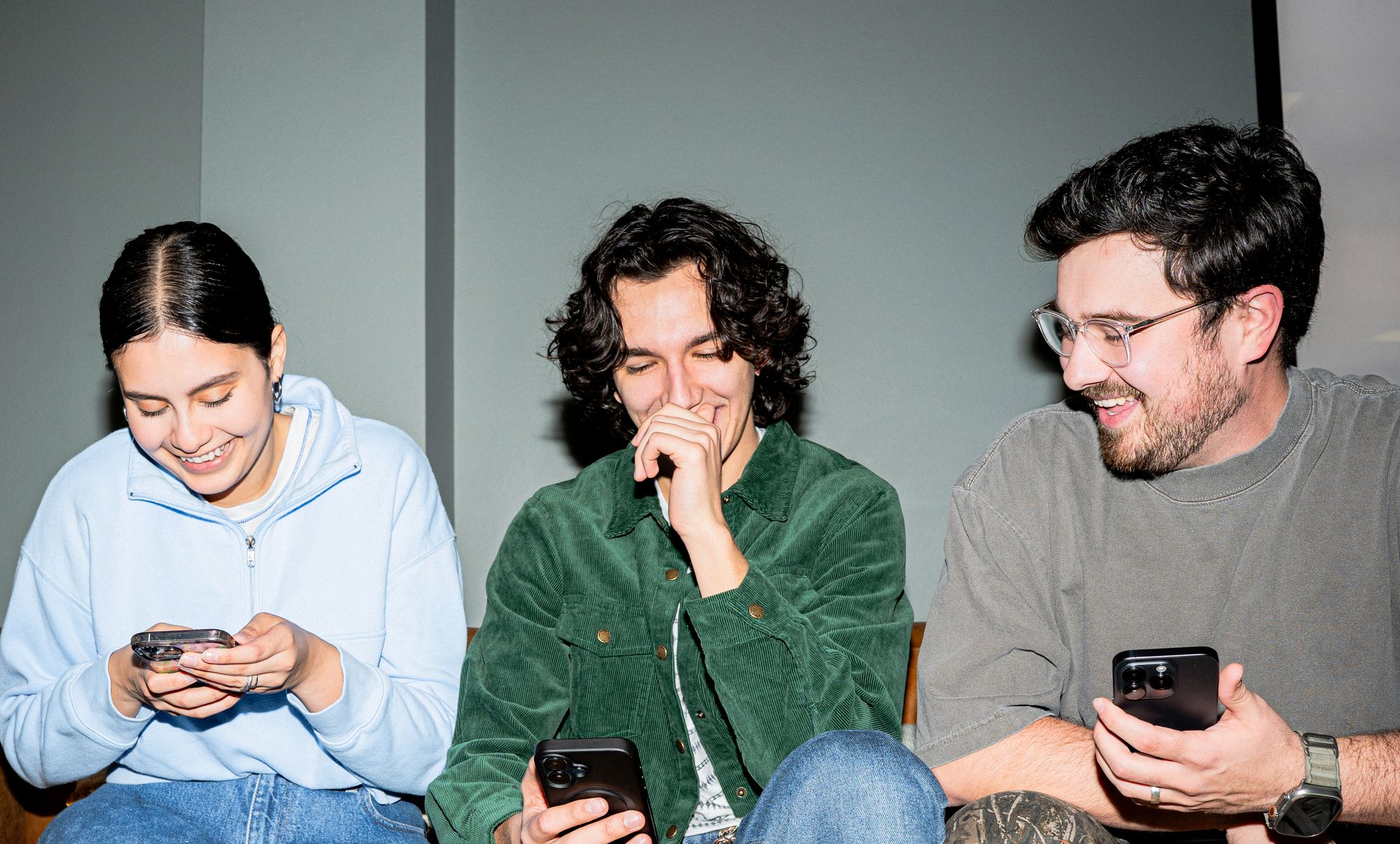 Three friends on a couch laughing at their phones, wearing googly eyes.